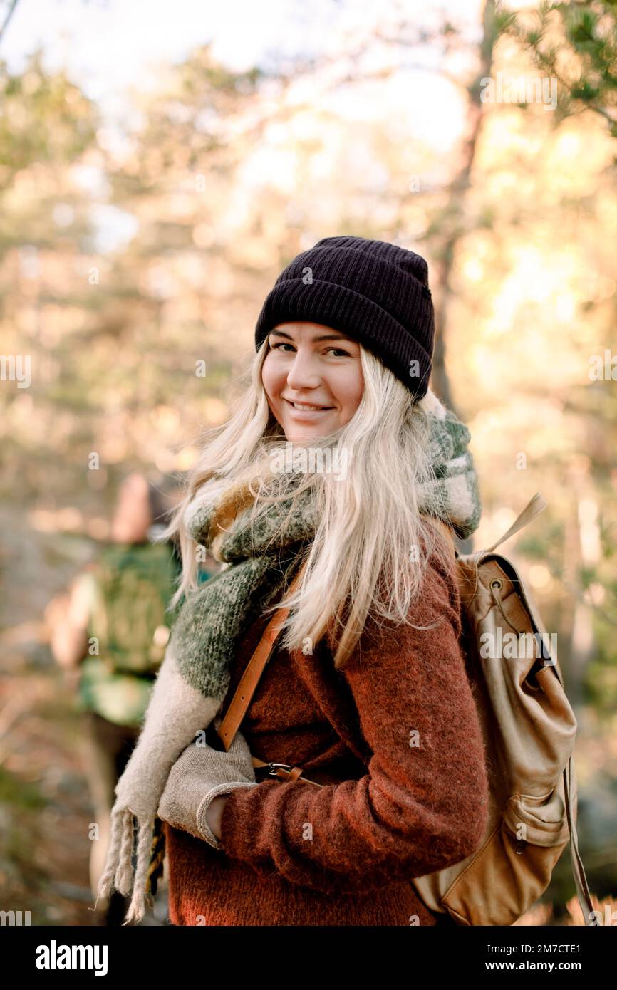 Seitenansicht einer lächelnden jungen Frau mit Rucksack im Wald Stockfoto