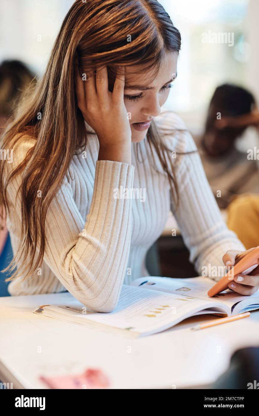 Trauriges Mädchen mit Kopf in der Hand, das am Schreibtisch ein Handy benutzt Stockfoto