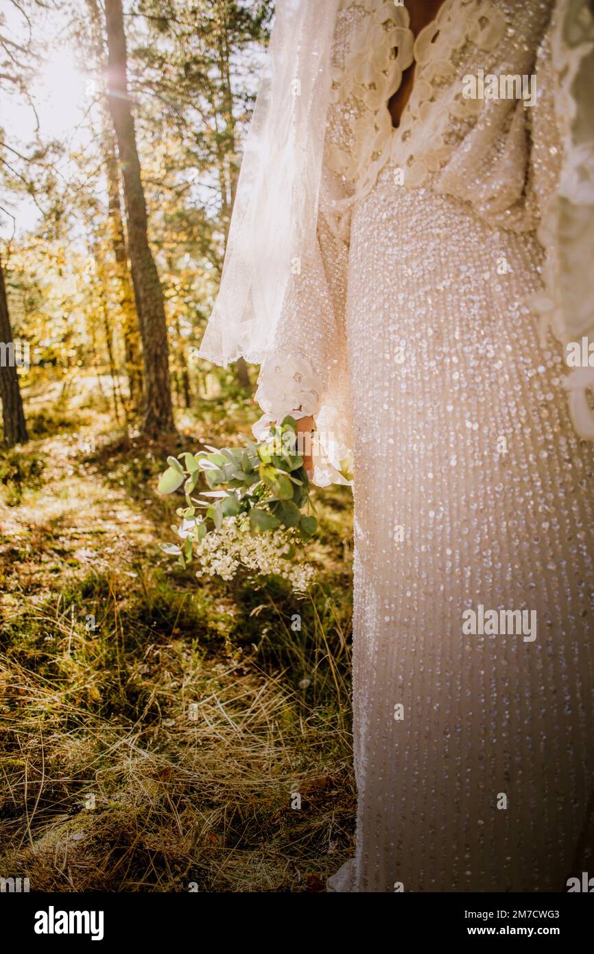 Mittelteil einer erwachsenen Braut, die im Wald ein weißes Hochzeitskleid trägt Stockfoto