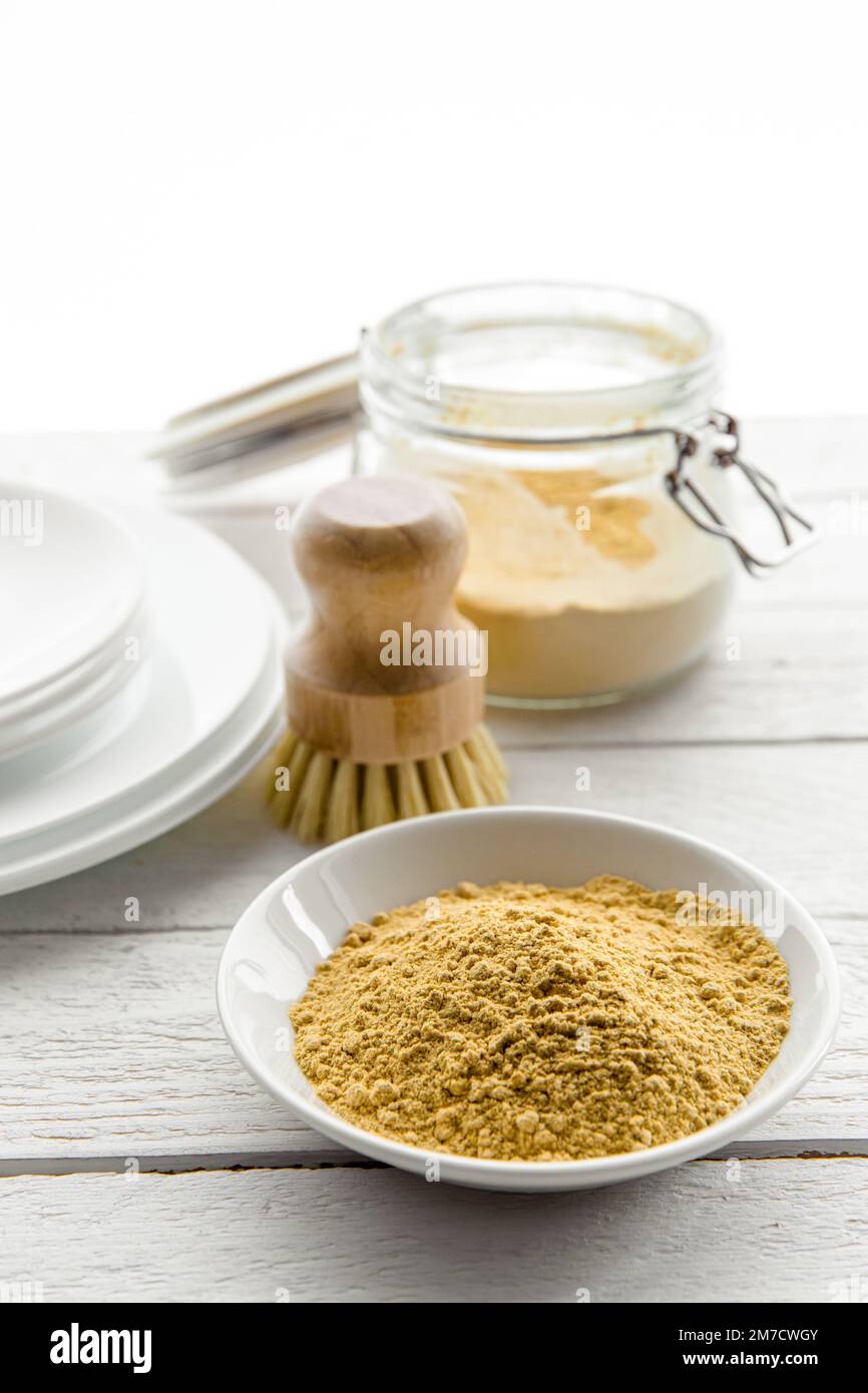 Geschirr mit Senfpulver spülen Konzept. Weiße, saubere Teller mit Schüssel und Becher mit gelbem Senfpulver und Geschirrspülbürste aus Holz. Stockfoto