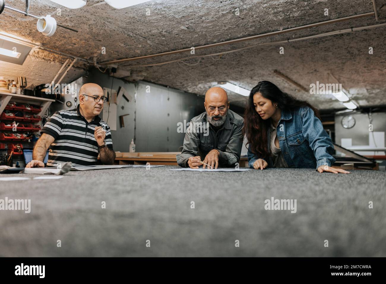 Ein Handwerker sieht einen männlichen Kollegen an, der mit einer Kundin auf der Werkbank über einen Entwurf spricht Stockfoto