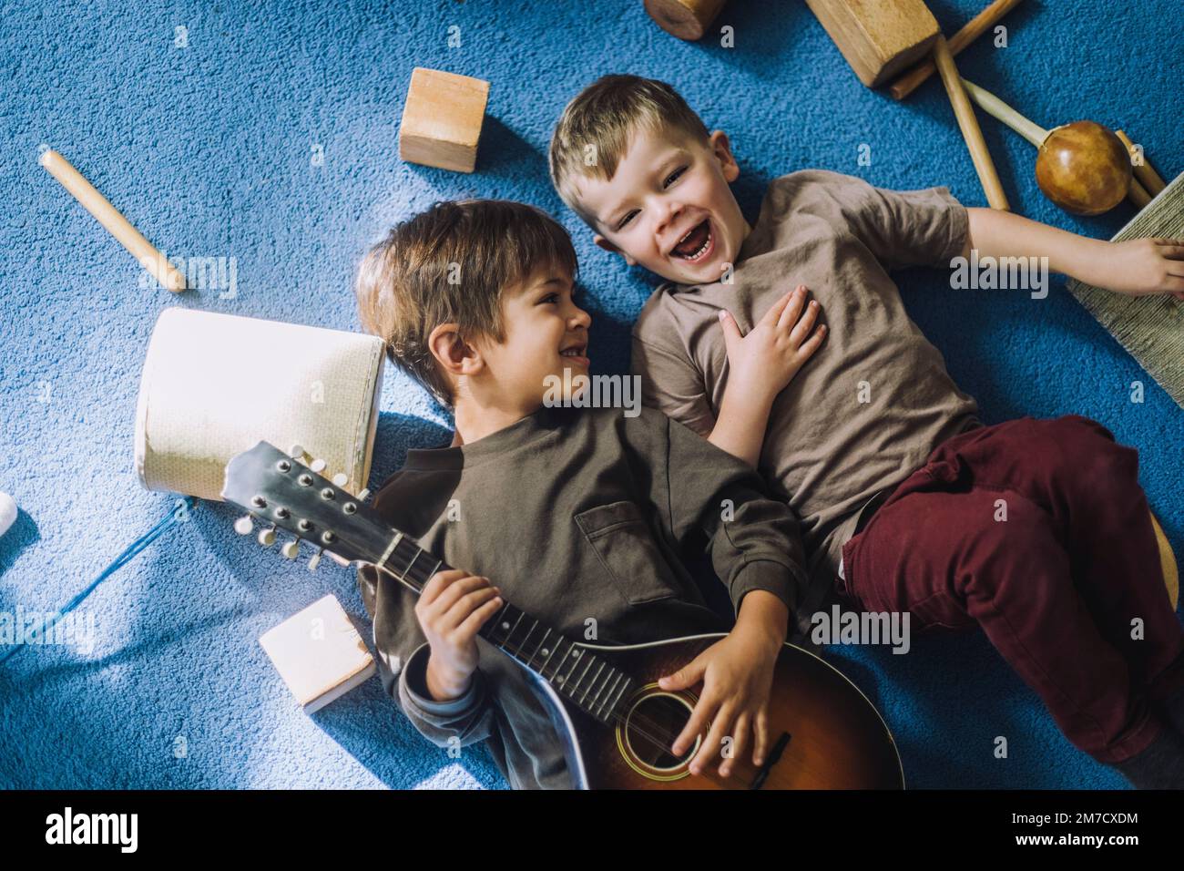 Fröhlicher Junge, der mit einem männlichen Klassenkameraden im Kindergarten Gitarre hält Stockfoto