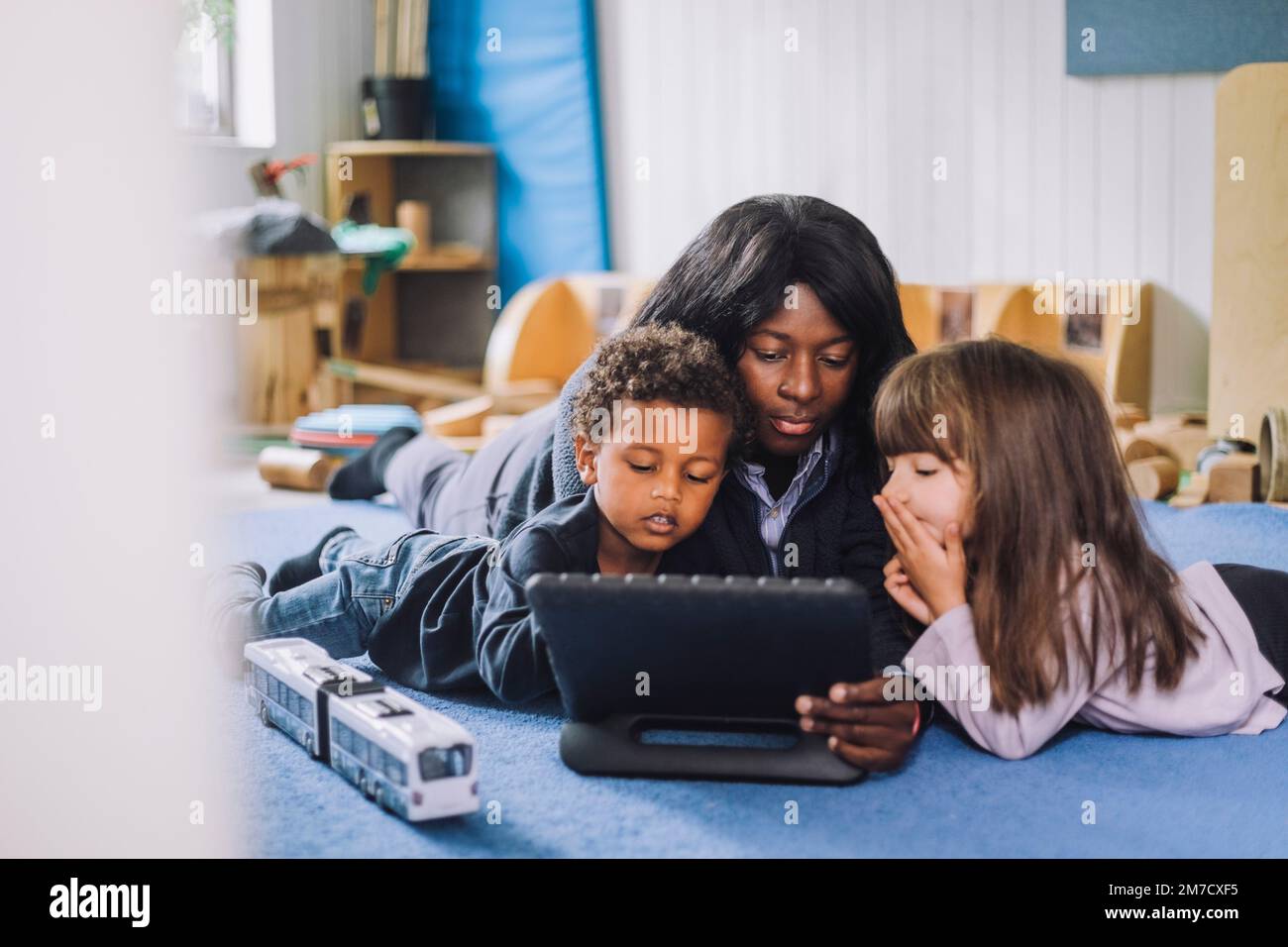 Kinderbetreuer, der ein digitales Tablet mit Schülern im Kindergarten teilt Stockfoto