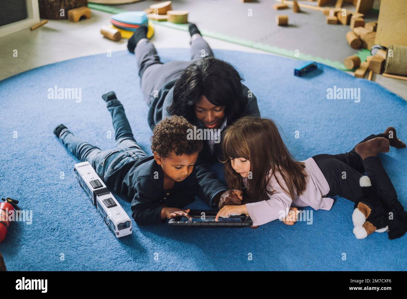 Lehrerin, die ein digitales Tablet mit Schülern in einer Kindertagesstätte benutzt Stockfoto