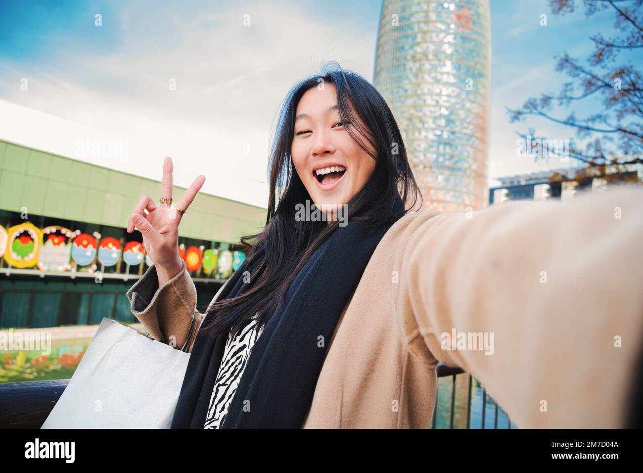 Glückliche junge asiatische Frau, die ein Selfie-Foto mit einem Smartphone macht. Selbstporträt einer lächelnden chinesin, die nach dem Einkaufen im Freien das Friedenszeichen trägt. Hochwertiges Foto Stockfoto