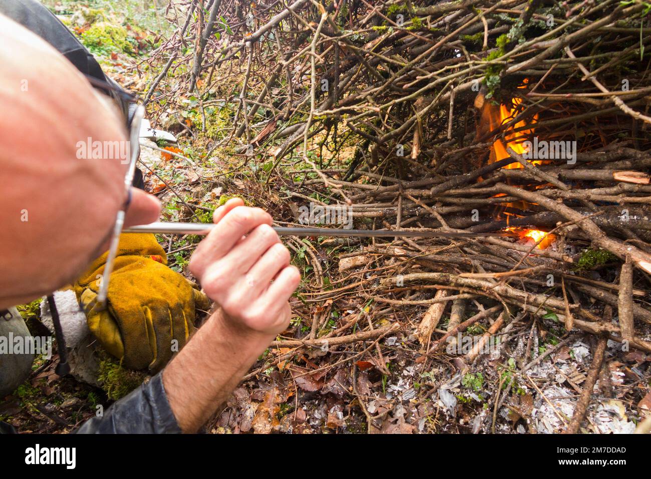 Fördern Sie das Feuer, indem Sie (Sauerstoff) ein sich ausdehnendes Metallrohr hinunterblasen, um die Flamme in einem häuslichen Lagerfeuer zu brennen, Blätter und Zweige zu verbrennen, die in einem häuslichen Garten auf dem Land angezündet werden. (133) Stockfoto