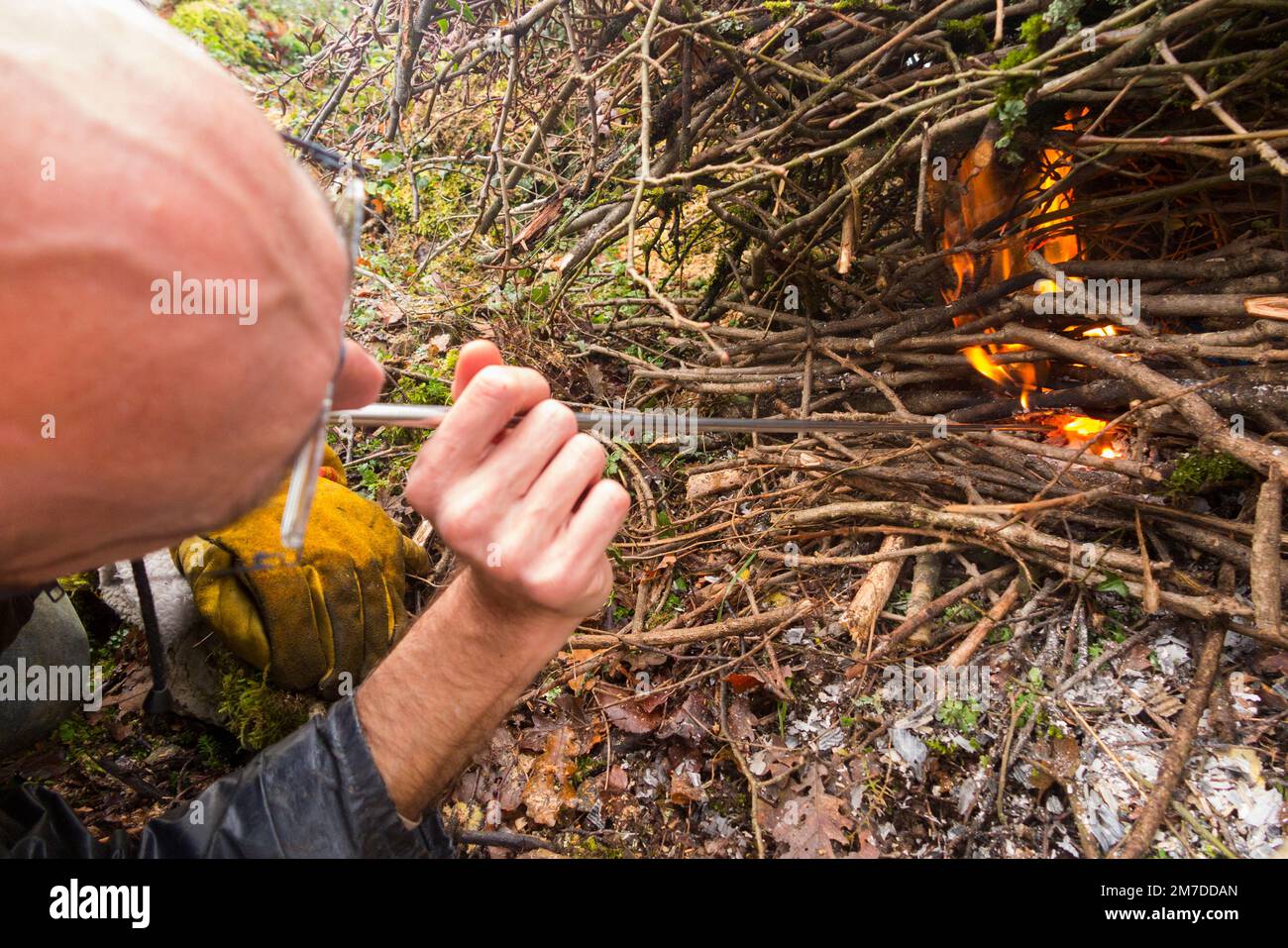 Fördern Sie das Feuer, indem Sie (Sauerstoff) ein sich ausdehnendes Metallrohr hinunterblasen, um die Flamme in einem häuslichen Lagerfeuer zu brennen, Blätter und Zweige zu verbrennen, die in einem häuslichen Garten auf dem Land angezündet werden. (133) Stockfoto