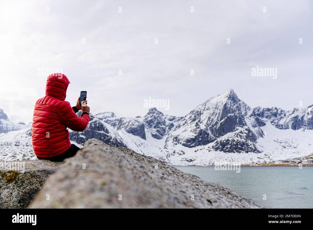 Mann, der im Winter mit Smartphone die gefrorene Landschaft fotografiert, Flakstadpollen, Nordland County, Lofoten-Inseln, Norwegen Stockfoto