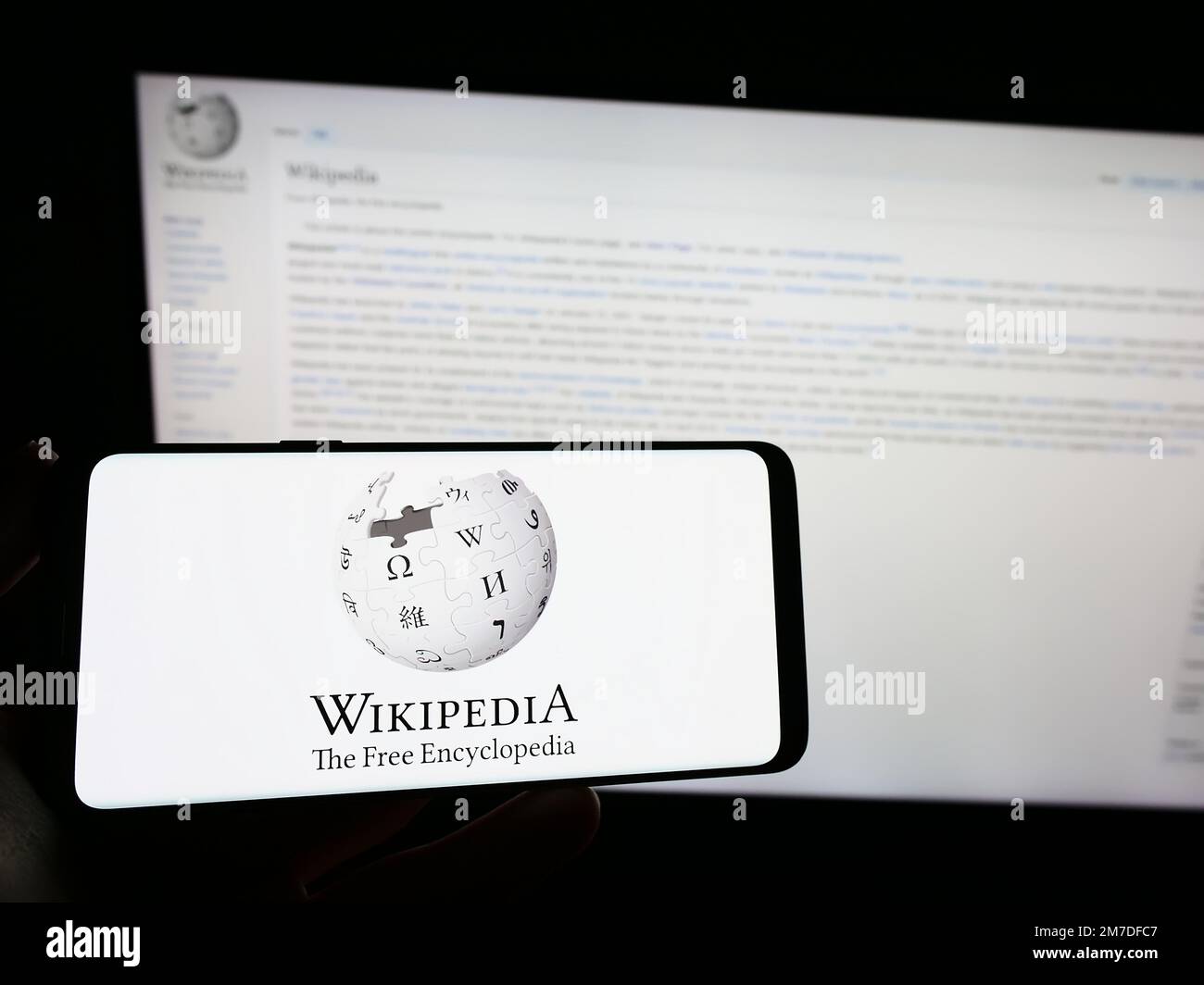 Person, die ein Smartphone mit dem Logo der Online-Enzyklopädie Wikipedia auf dem Bildschirm vor der Website hält. Konzentrieren Sie sich auf das Display des Telefons. Stockfoto