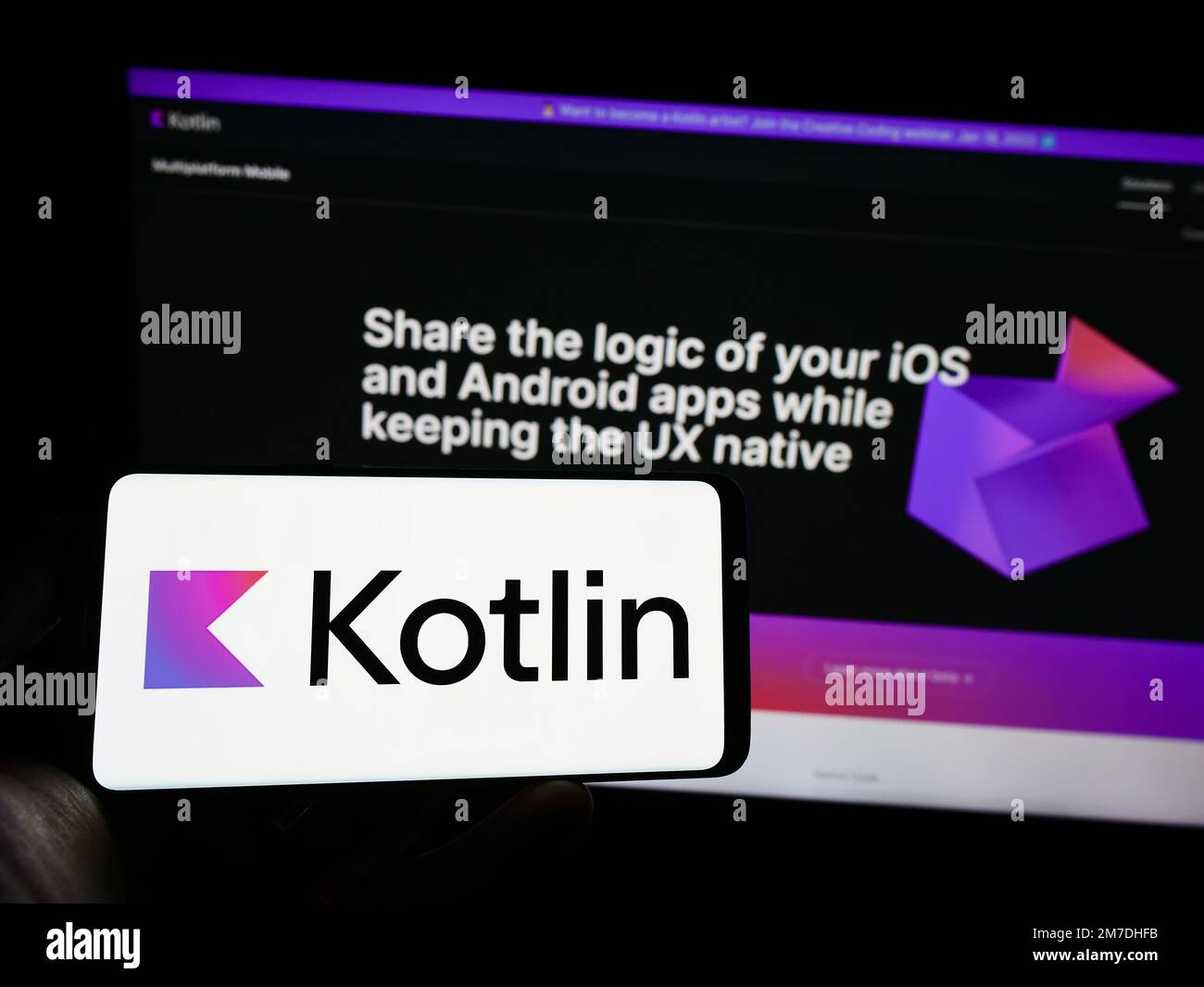 Person mit Mobiltelefon mit Logo der Programmiersprache Kotlin auf dem Bildschirm vor der Webseite. Konzentrieren Sie sich auf das Display des Telefons. Stockfoto