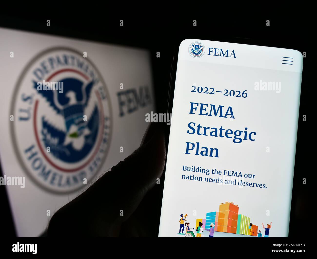 Person, die ein Handy mit der Webseite der Federal Emergency Management Agency (FEMA) auf dem Bildschirm vor dem Siegel hält. Konzentrieren Sie sich auf die Mitte des Telefondisplays. Stockfoto