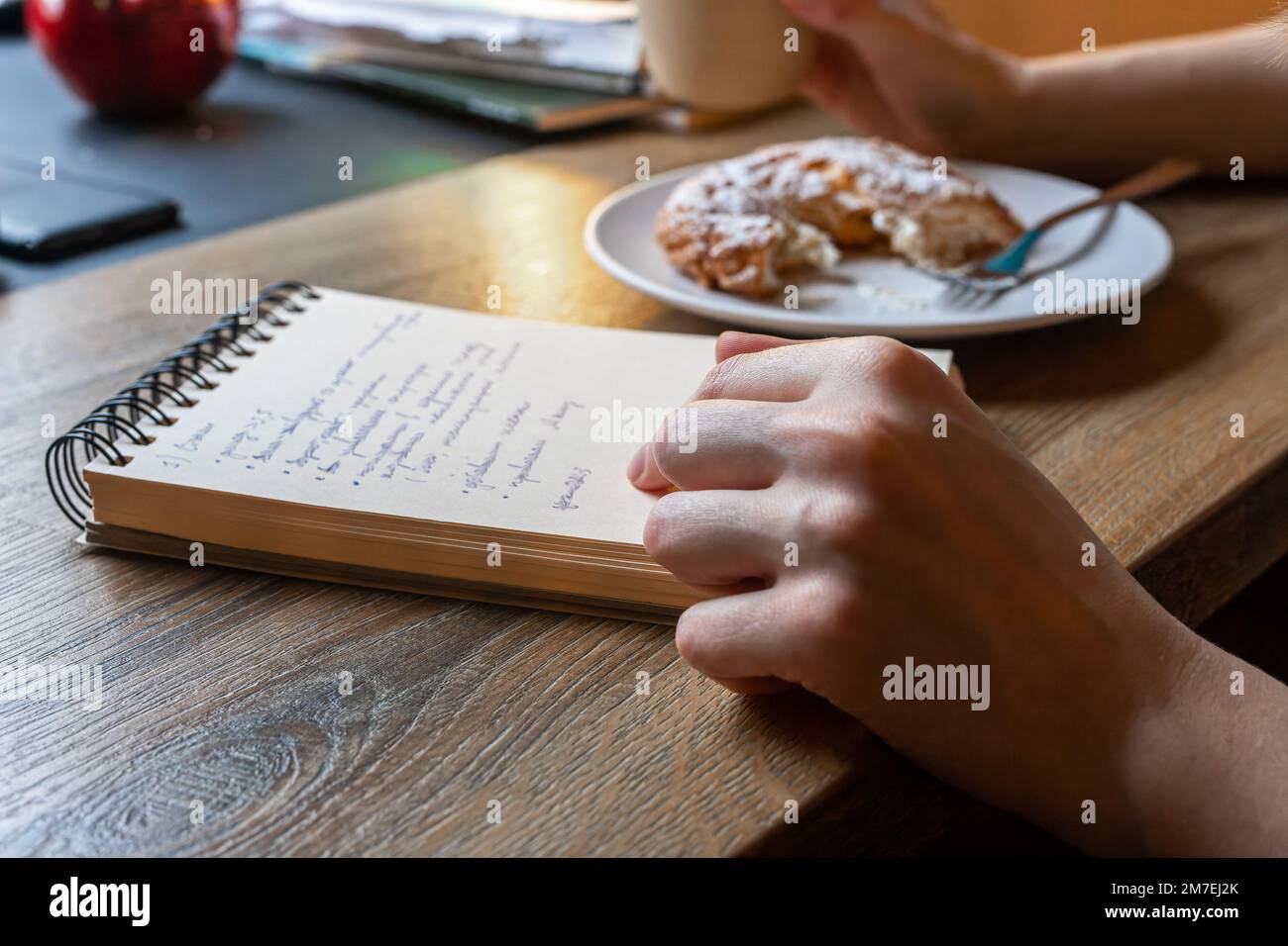 Hand mit Notizblock am Cafétisch, Holzschreibtisch, Pläne schreiben, Ziele in Planer, Notizblock, Organisator setzen. Hochwertiges Foto Stockfoto