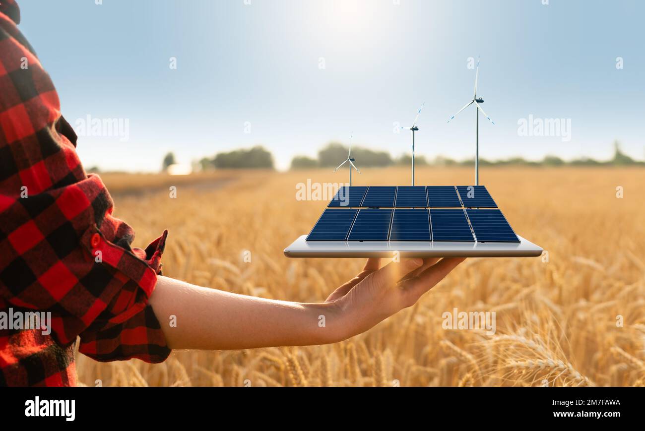 Farmer hält ein digitales Tablet mit Solarpaneelen und Windturbinen. Konzept der nachhaltigen Landwirtschaft Stockfoto