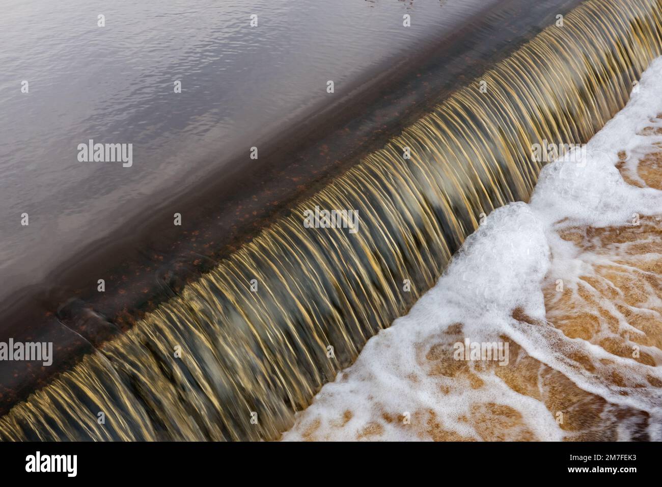 Eisenhaltiges Wasser fließt schäumend über einen Damm, der für die Wasserstandsanpassung gebaut wurde Stockfoto