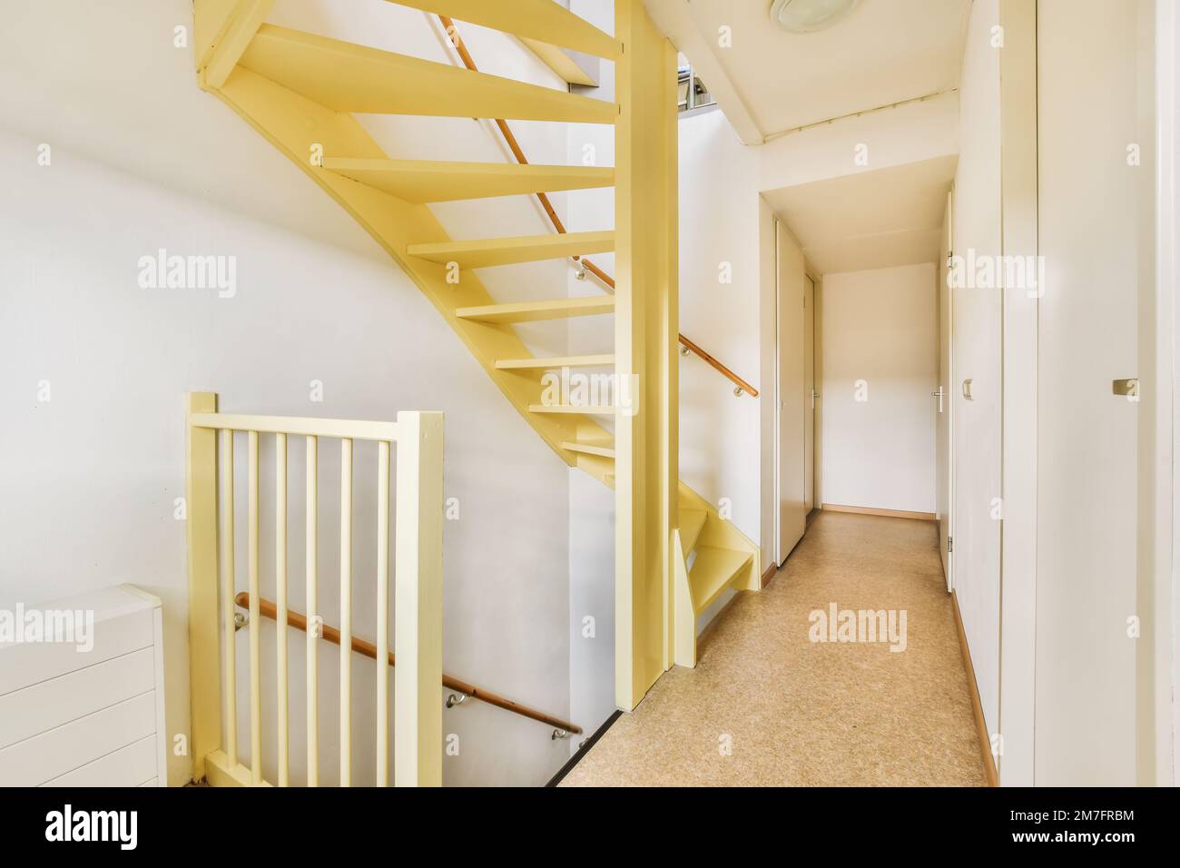 Ein Flur in einem Appartement mit weißen Wänden und gelber Treppe, die in die zweite Etage führt, es gibt eine Uhr an der Wand Stockfoto