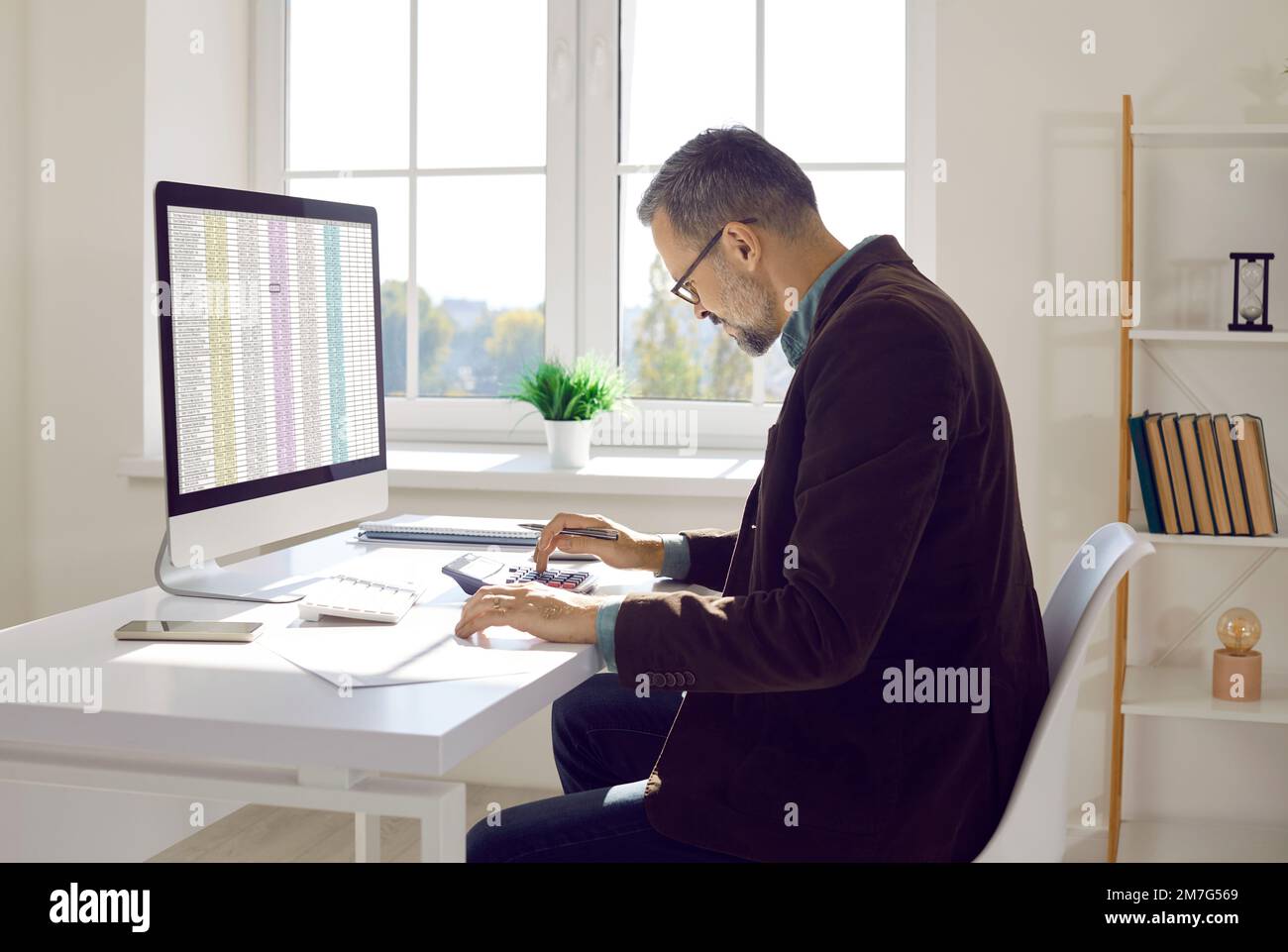 Finanzbuchhalter sitzt am Schreibtisch, arbeitet am Computer und verwendet Taschenrechner Stockfoto
