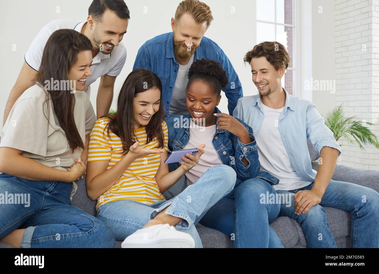 Gruppe von Personen zu Hause, die zusammen lustige Fotos und Videos auf dem Mobiltelefon ansehen. Stockfoto