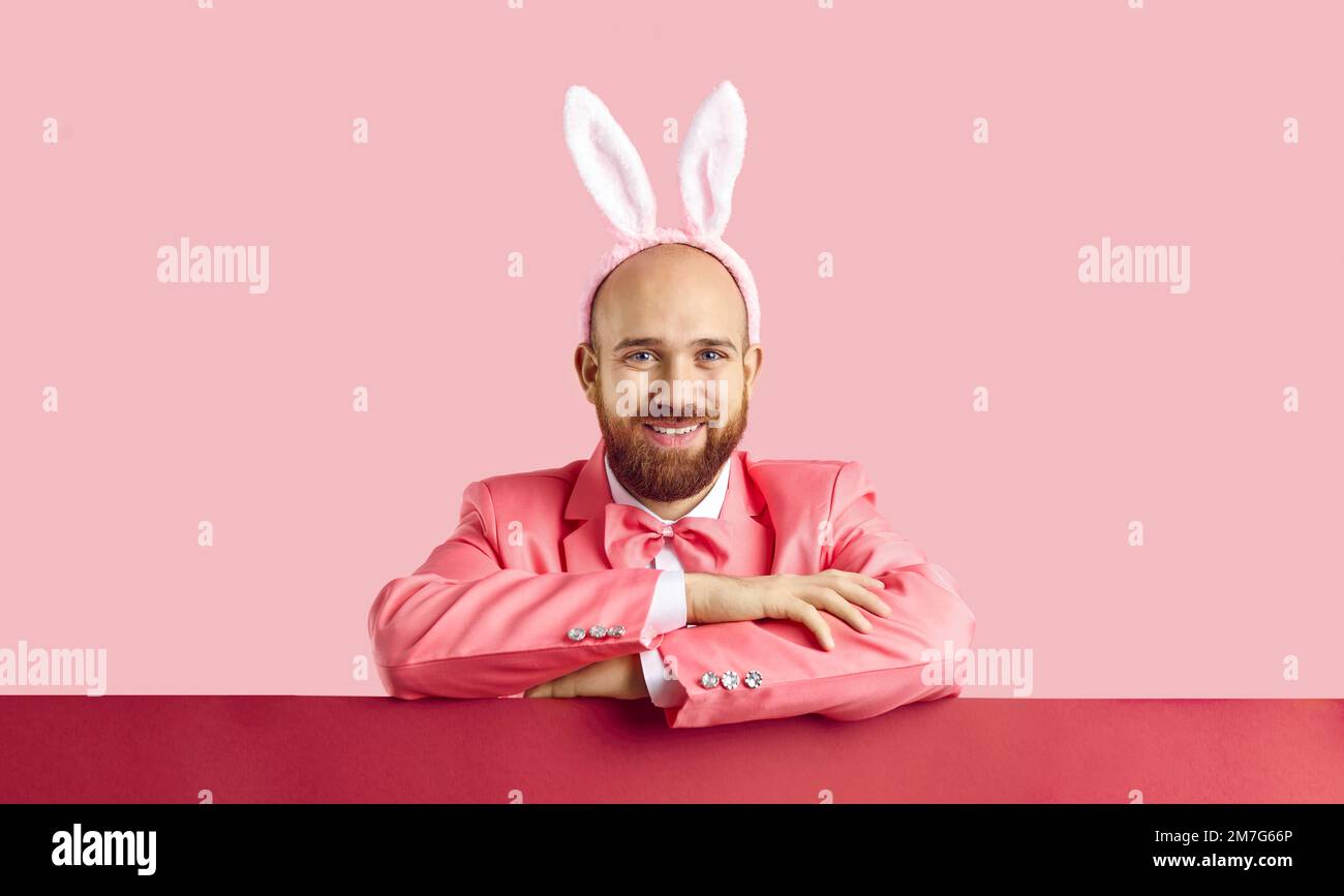 Studioporträt eines fröhlichen, gutaussehenden Mannes mit pinkfarbenem Anzug und Osterhäschen-Ohren Stockfoto