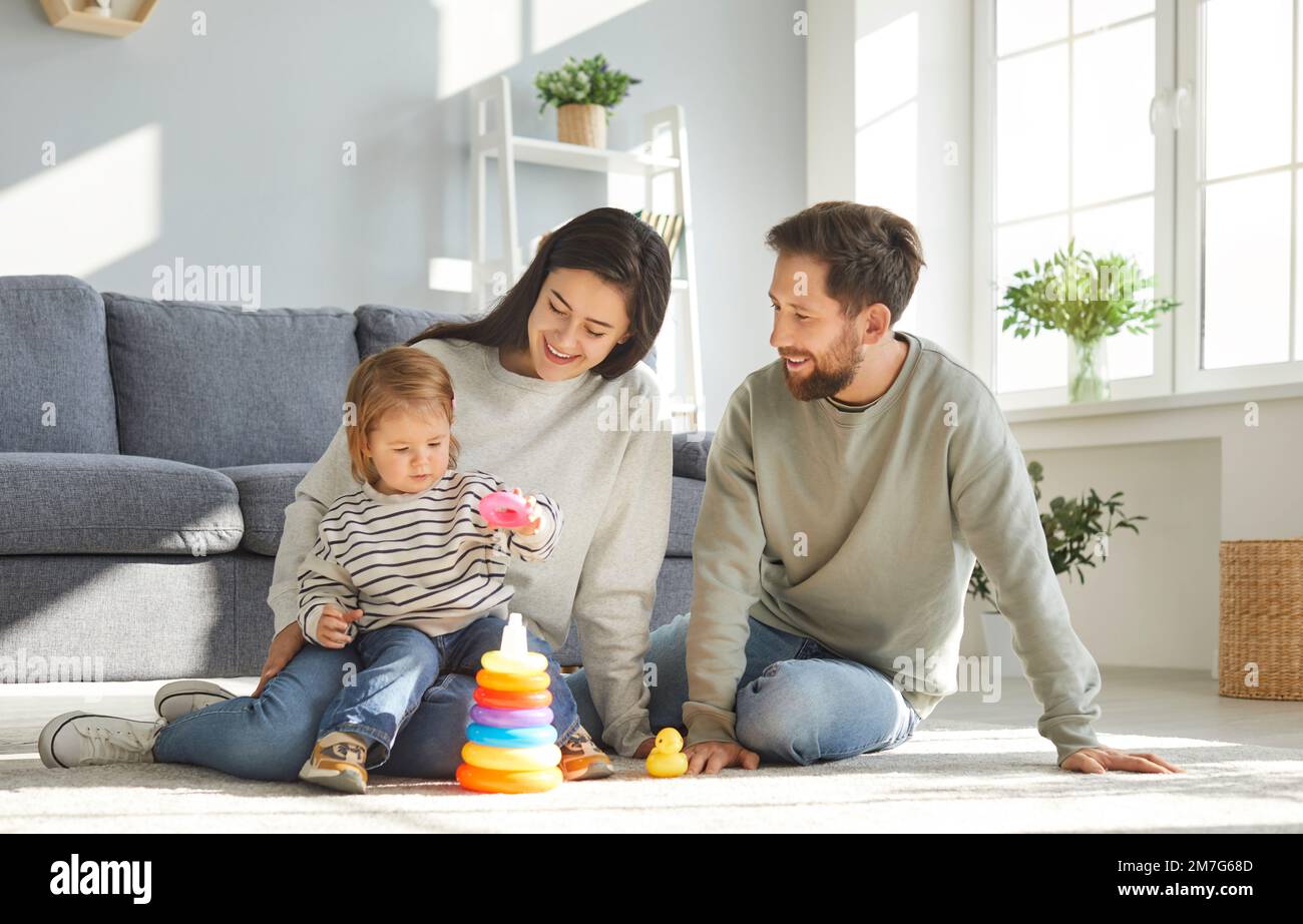 Die Familie baut mit ihrer kleinen Tochter einen Regenbogenturm, während sie auf dem Boden des Kinderzimmers spielt. Stockfoto