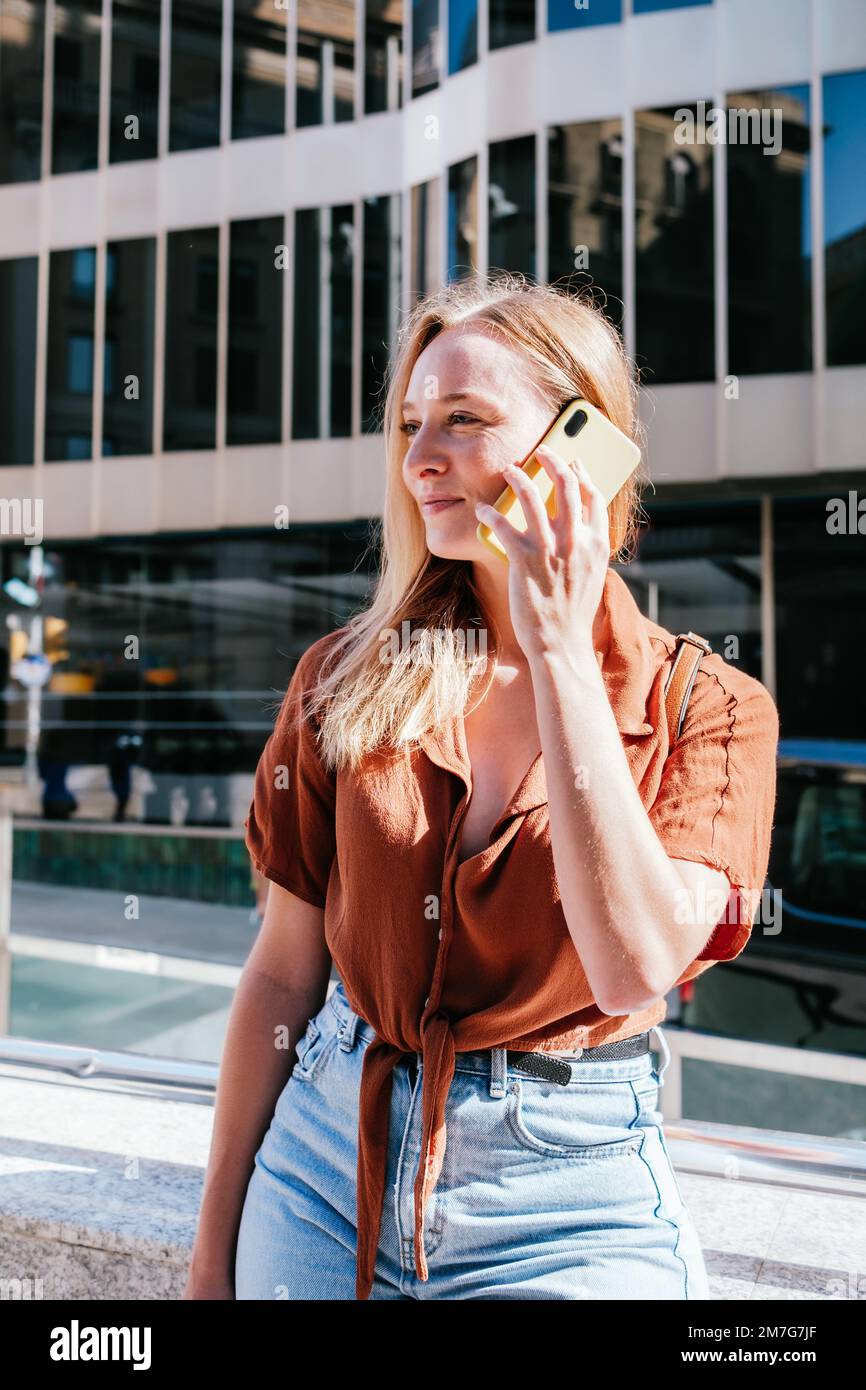 Junge Weiße, die draußen wartet und ihr Telefon benutzt. Sie hat Bürogebäude im Hintergrund Stockfoto