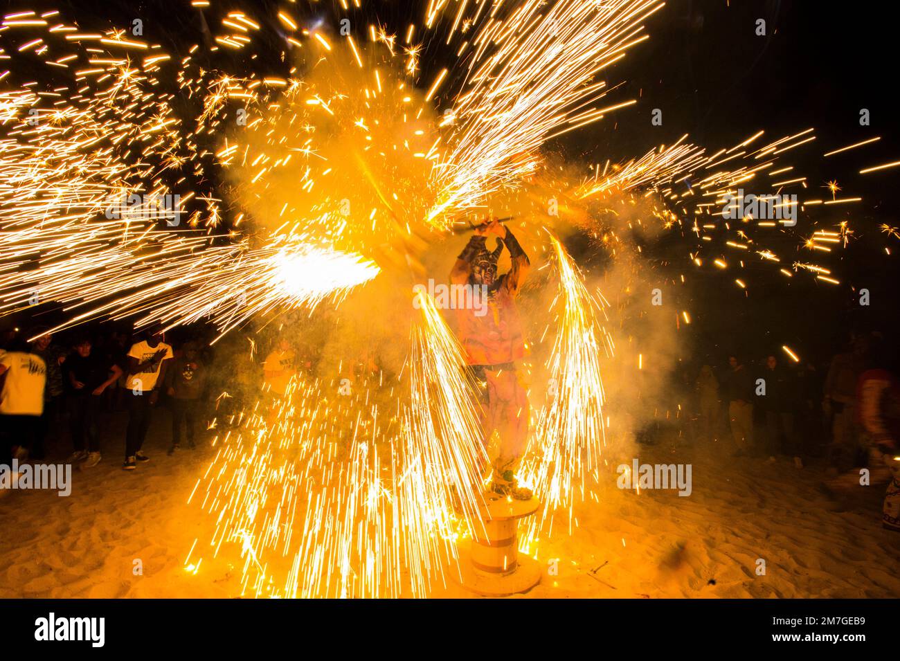 Feuerwerk am Strand von Porto Cristo. Jugendliche, die als Dämonen verkleidet sind, winken mit Feuerwerk um sie herum. Stockfoto