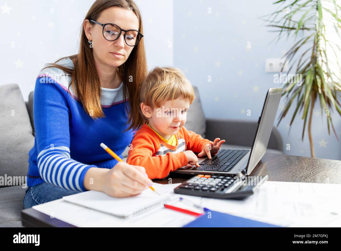 Junge Frau, die zu Hause mit einem Laptop arbeitet und ein Kind auf dem Schoß hat Stockfoto