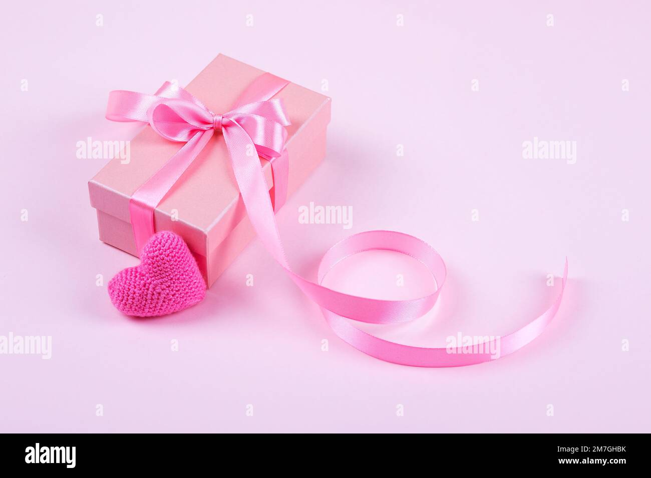 Grußkarte zum Valentinstag, Muttertag und Geburtstag. Gestricktes rosa Herz und Geschenkbox mit Schleife aus Satin auf pinkfarbenem Hintergrund Stockfoto