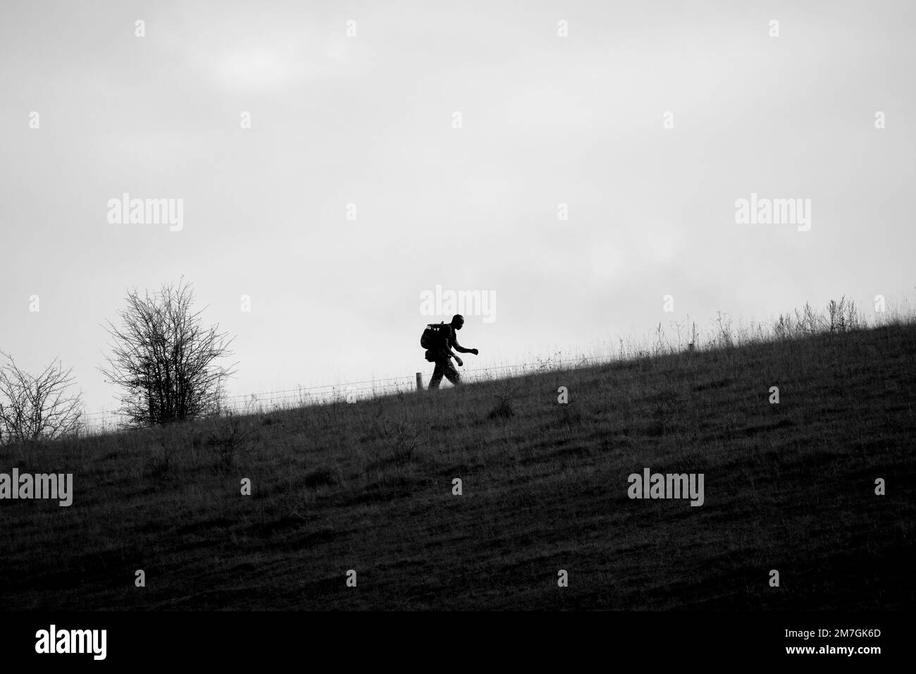 Silhouette eines Armeesoldaten, der einen steilen Hügel mit 40kg bergen über offene Landschaften in Wiltshire UK hinaufrutscht Stockfoto