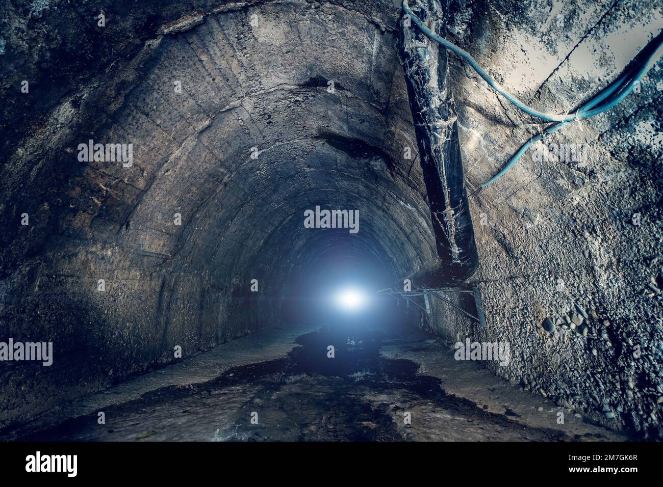 Abwasser im großen unterirdischen Abwassertunnel. In einem dunklen städtischen Abwasserkanal-Tunnel mit Licht am Ende Stockfoto