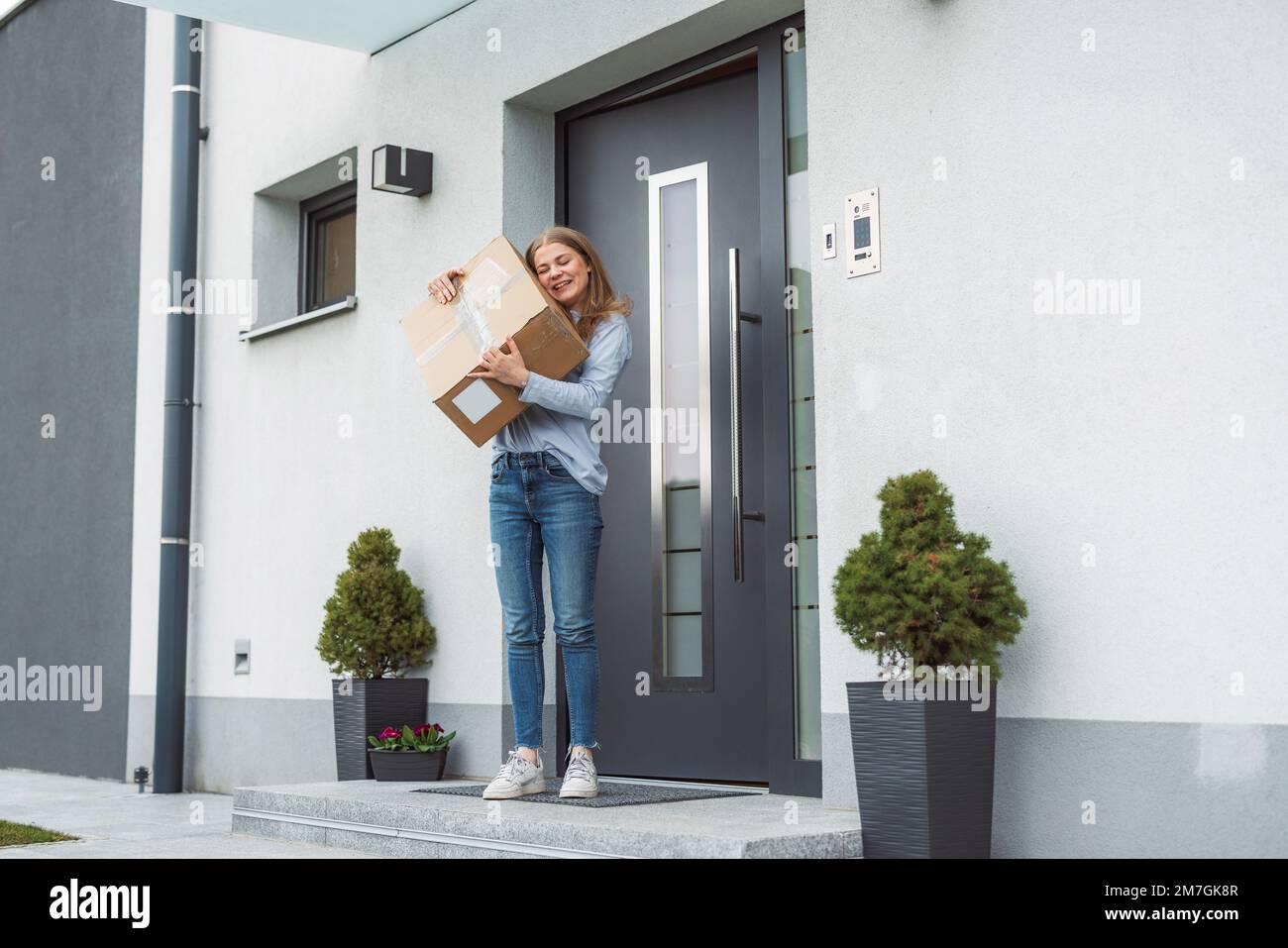 Eine glückliche junge Frau mit einem Postboten aus Pappe, die gerade an ihre Haustür gebracht wurde Stockfoto