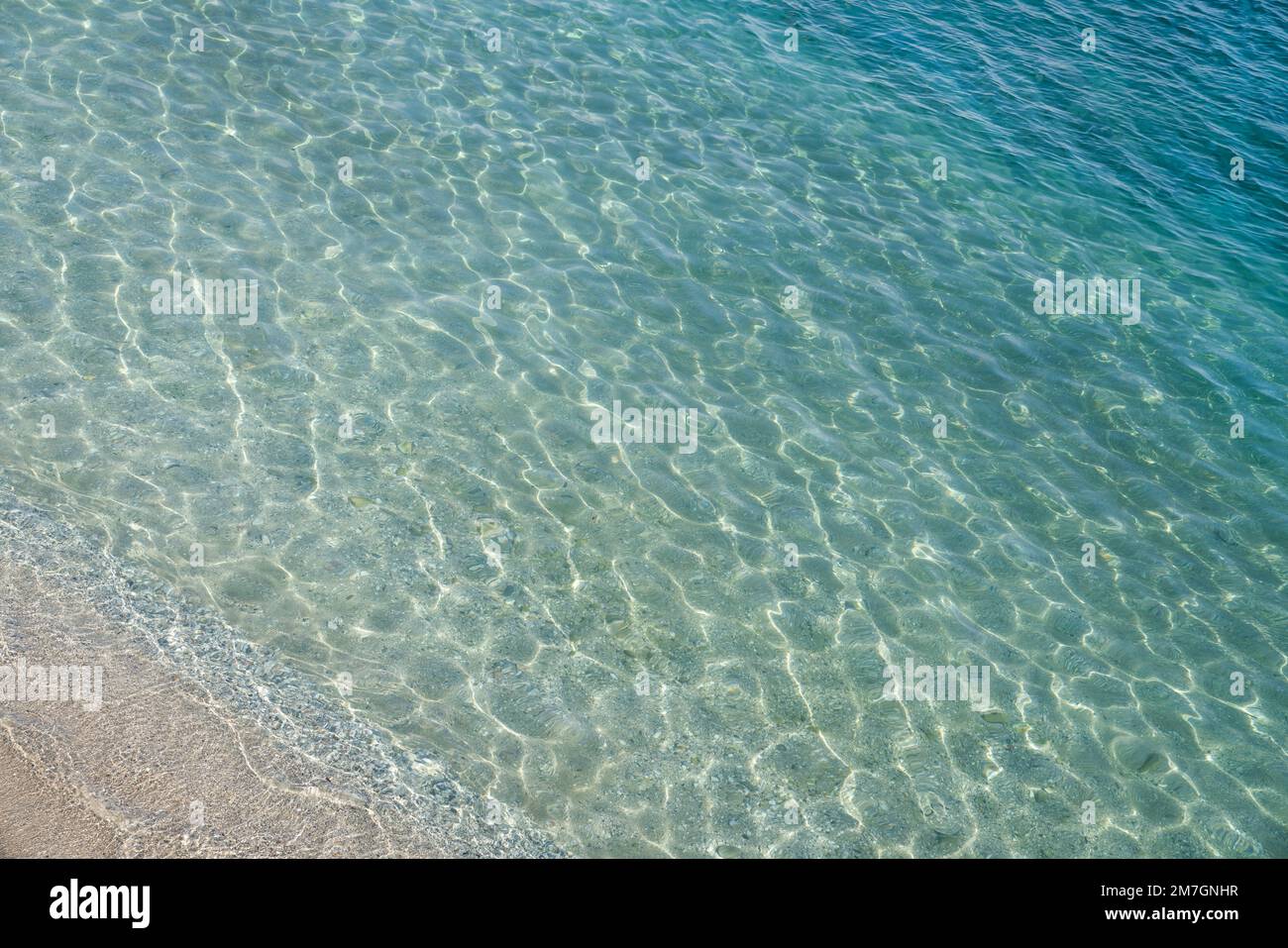 Sandstrand, der unter die Meersoberfläche des Wassers führt. Wunderschöner Farbverlauf von blassblauer Farbe. Sonnenblende auf der Wasseroberfläche Stockfoto