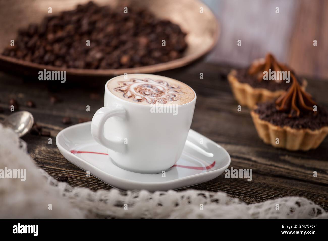 Aromatischer frisch gebrühter Kaffee auf einem Hintergrund aus Kaffeebohnen und cremigen Keksen. Café-Atmosphäre Stockfoto