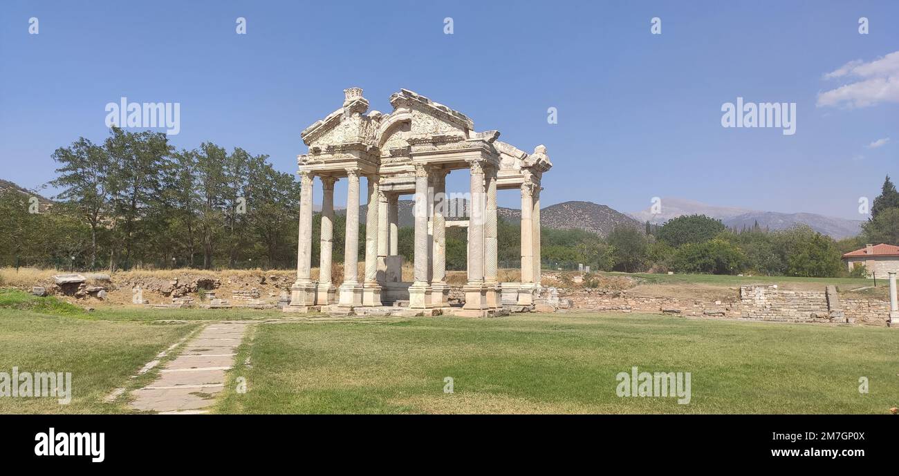 Die Ruine der antiken griechisch-hellenistischen Stadt in Westanatolien, Türkei, auf einem grasbedeckten Feld mit Bäumen und Bergen im Hintergrund Stockfoto