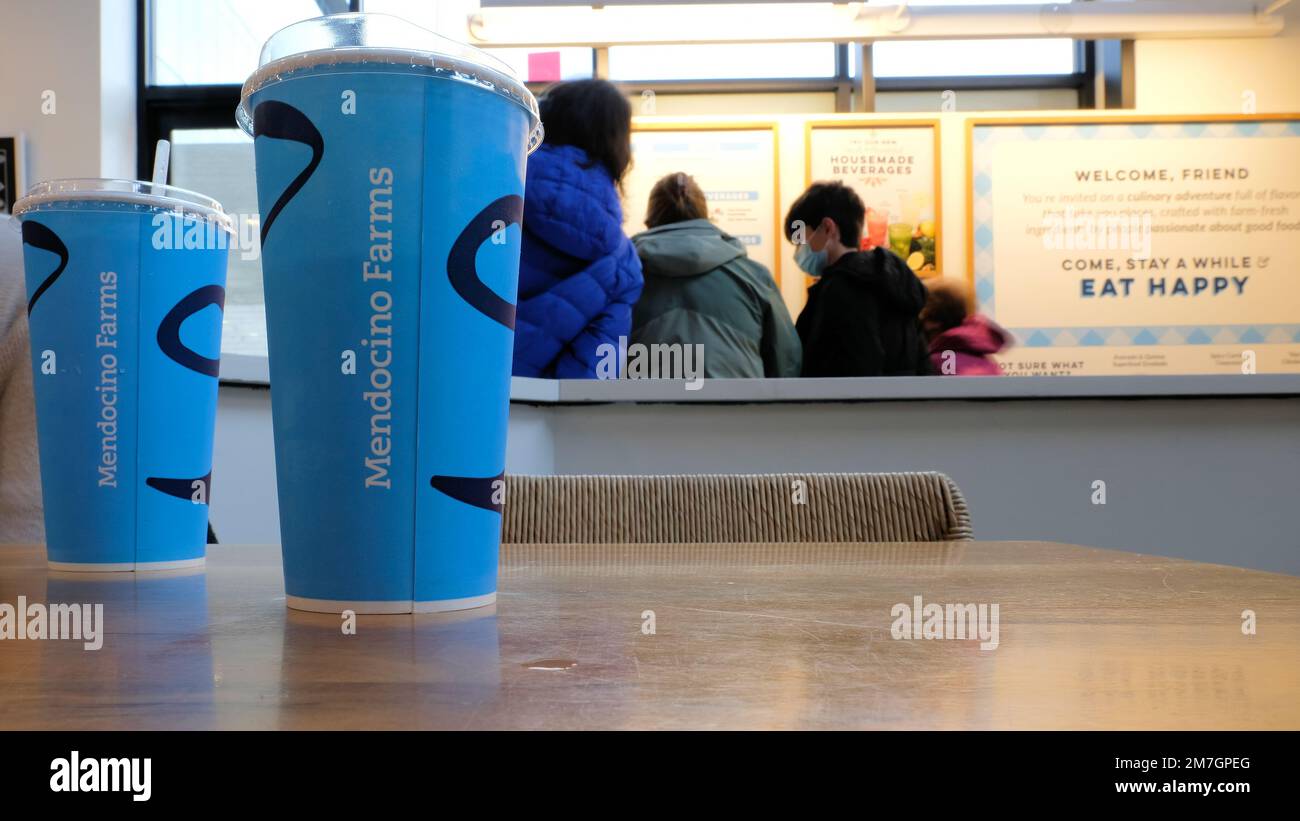 Zwei Getränketassen auf einem Tisch, während Gäste im Hintergrund die Speisekarte und die Speisemöglichkeiten eines Sandwichgeschäfts der Mendocino Farms in San Jose, Kalifornien, betrachten Stockfoto