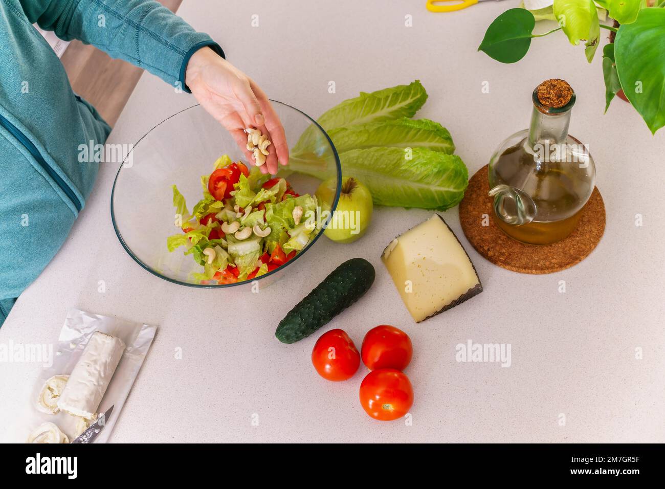 Frau, die Cashews zu einem gesunden Salat an ihrem Küchentisch hinzufügt Stockfoto