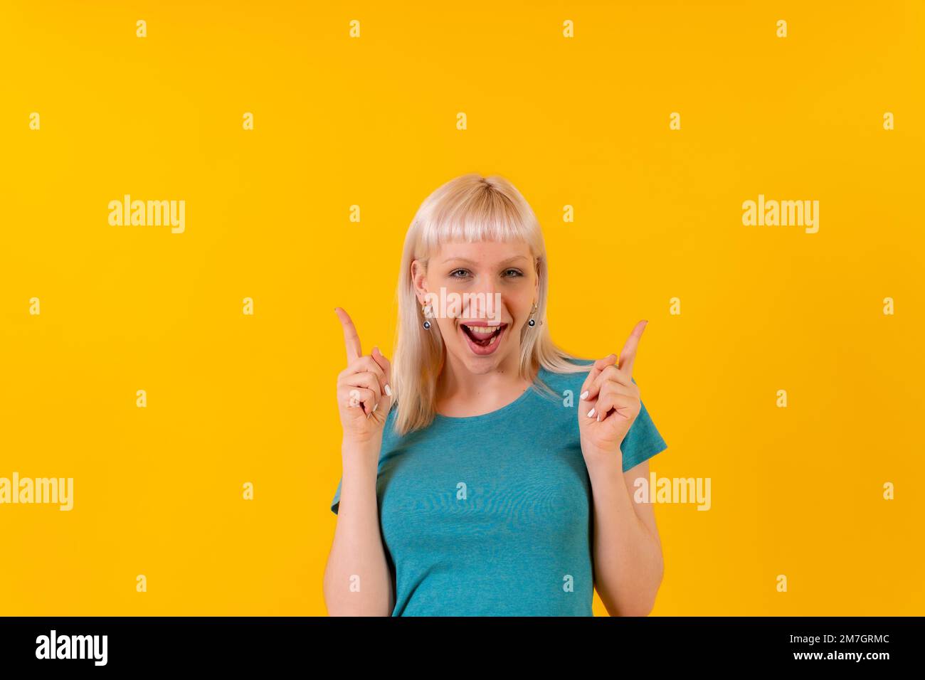 Ein lächelndes Porträt, das nach oben zeigt, ein blondes, weißes Mädchen im Studio auf gelbem Hintergrund Stockfoto