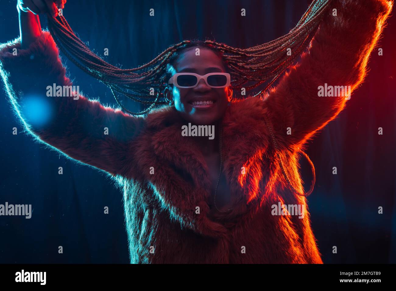 Schwarze ethnische Frau mit Zöpfen mit blauen und roten LED-Lichtern, die ihr Haar beim Tanzen bewegt Stockfoto