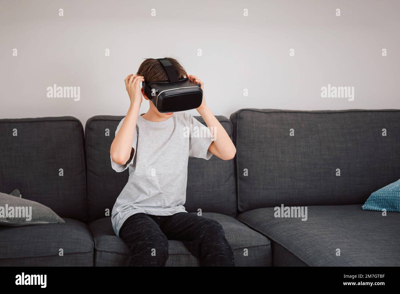 Männliches Kind aus Kaukasien, das ein Virtual-Reality-Headset aufsetzt und überrascht von einer virtuellen Welt aussieht Stockfoto