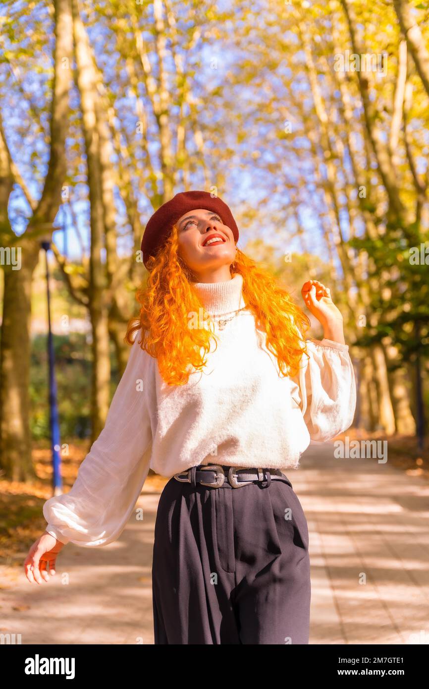 Porträt einer rothaarigen Frau in einer Baskenmütze, die bei Sonnenuntergang durch einen Stadtwaldpark läuft Stockfoto