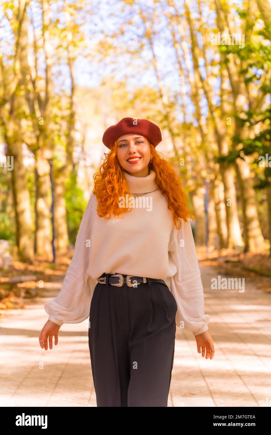 Eine rothaarige Frau in einer Baskenmütze, die bei Sonnenuntergang durch einen Stadtwaldpark läuft Stockfoto