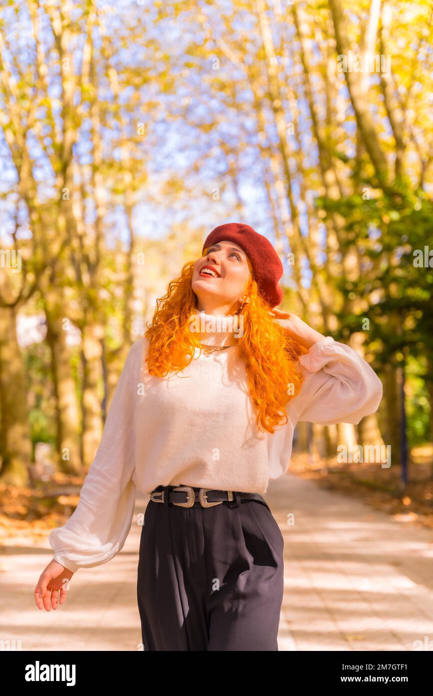 Rothaarige Frau in einer Baskenmütze, die bei Sonnenuntergang durch einen Stadtwaldpark läuft, vertikales Foto Stockfoto