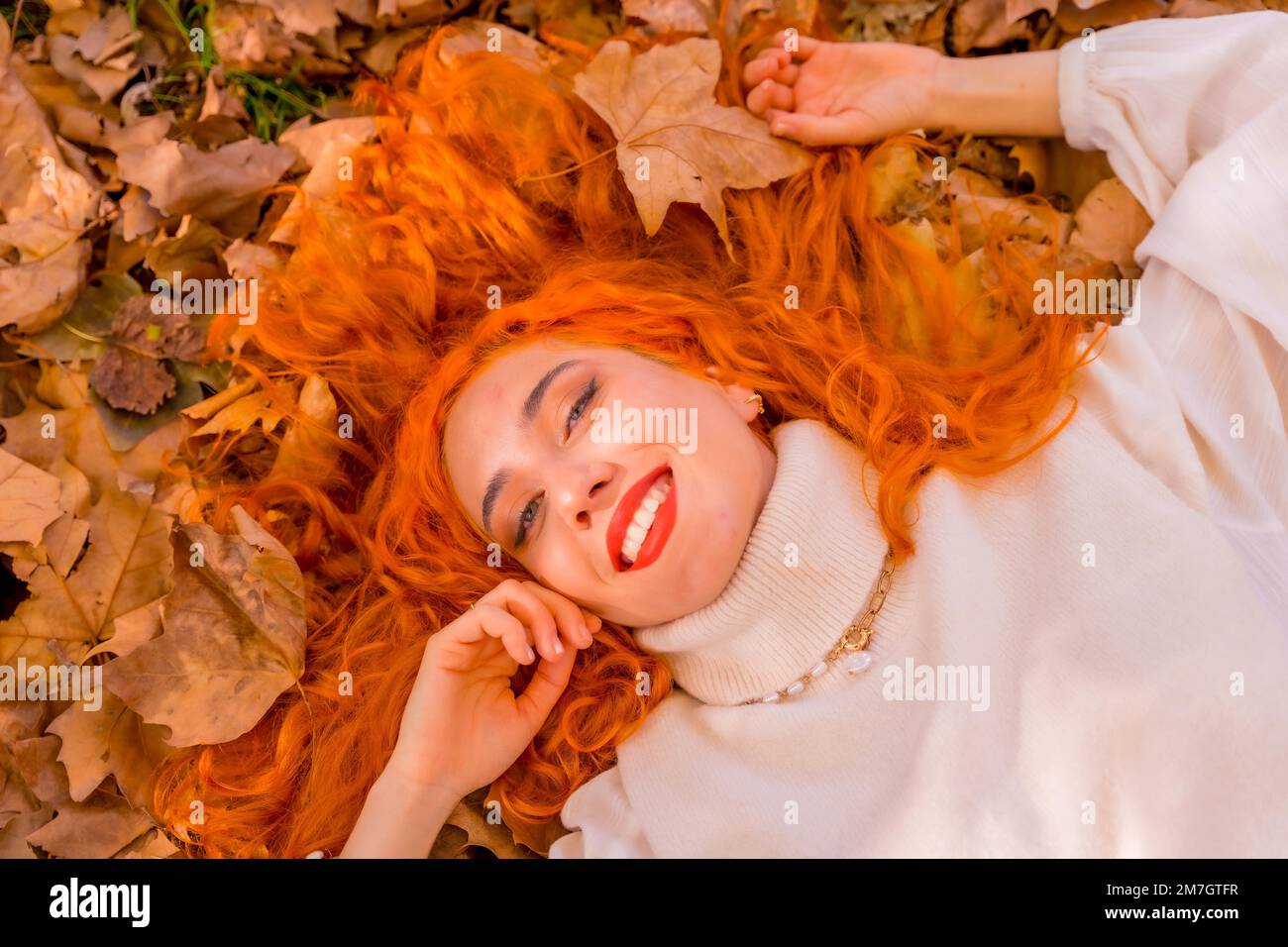 Rothaarige Frau liegt auf Blättern im Stadtpark und lächelt, Herbstsaison Lebensstil Stockfoto