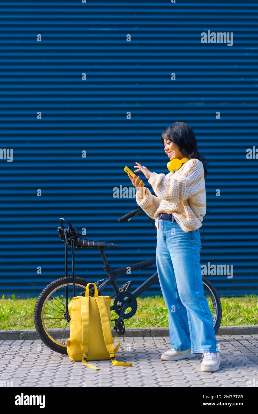 Asiatische Studentin, die Musik mit gelben Kopfhörern auf blauem Hintergrund hört Stockfoto