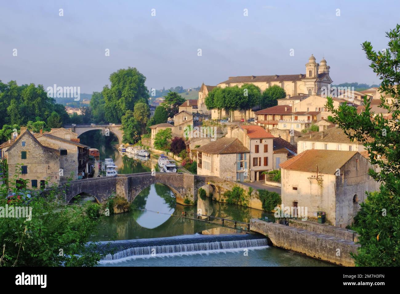 Nerac: Kirche Saint-Nicolas, Stadt, Kanalboote, Brücken und Fluss Petit Baise mit Spiegelreflexionen kurz nach Sonnenaufgang in Nerac, Frankreich Stockfoto