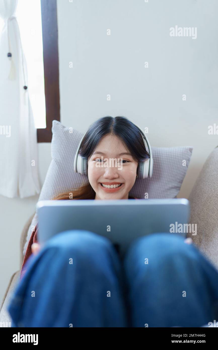 Porträt einer asiatischen Frau, die Tablet und Kopfhörer zu Hause auf dem Sofa entspannt Stockfoto