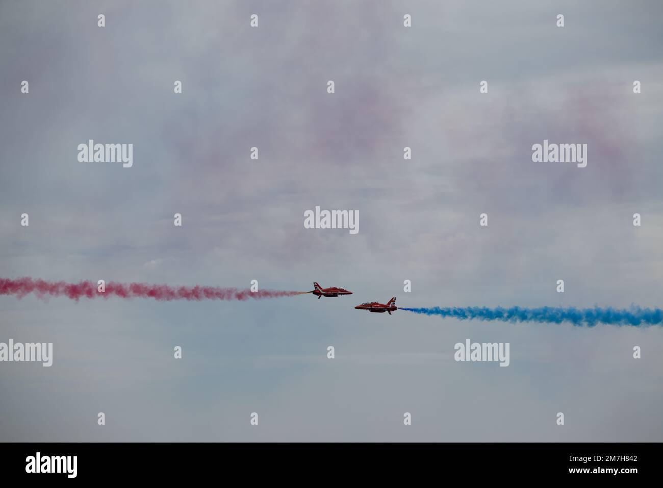 Zwei Flugzeuge der Serie BAE Systems Hawk T1 mit roten Pfeilen führen ein Kreuzmanöver durch und führen roten und blauen Rauch auf einer Ausstellung über Eastbourne, East Sussex, durch Stockfoto