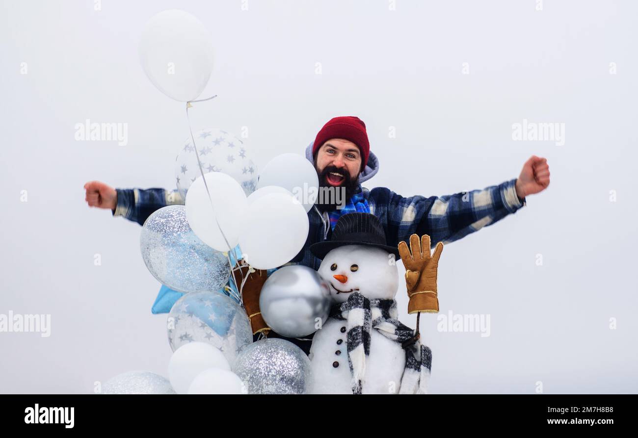 Frohe Feiertage. Bärtiger Mann im Winter mit Schneemann im Hut, Schal und Fäustlingen mit Luftballons. Stockfoto