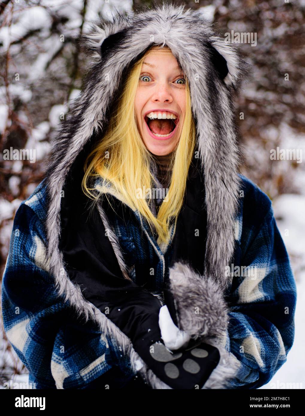 Lächelndes Mädchen in warmer Kleidung mit Schneeball. Schöne junge Frau, die im Winterpark mit Schnee spielt. Stockfoto