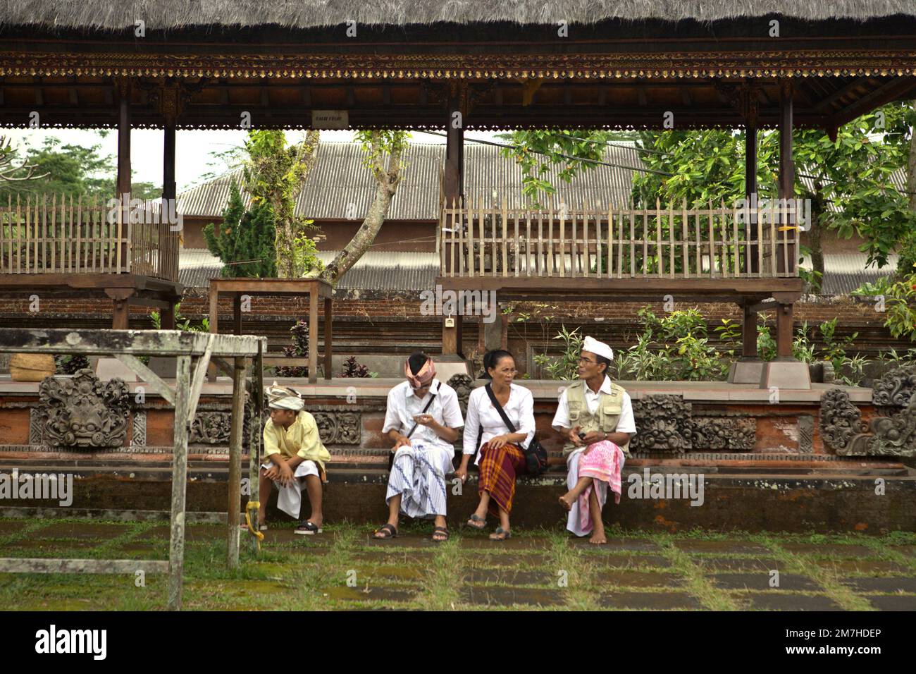 Eine Familie ruht sich aus und hält an einer Prozession, um die Geister ihrer verstorbenen Familienmitglieder zu ehren und zu reinigen, in der Nähe eines Tempels in der Besakih-Tempelanlage, am Hang des Agung in Karangasem, Bali, Indonesien. Stockfoto