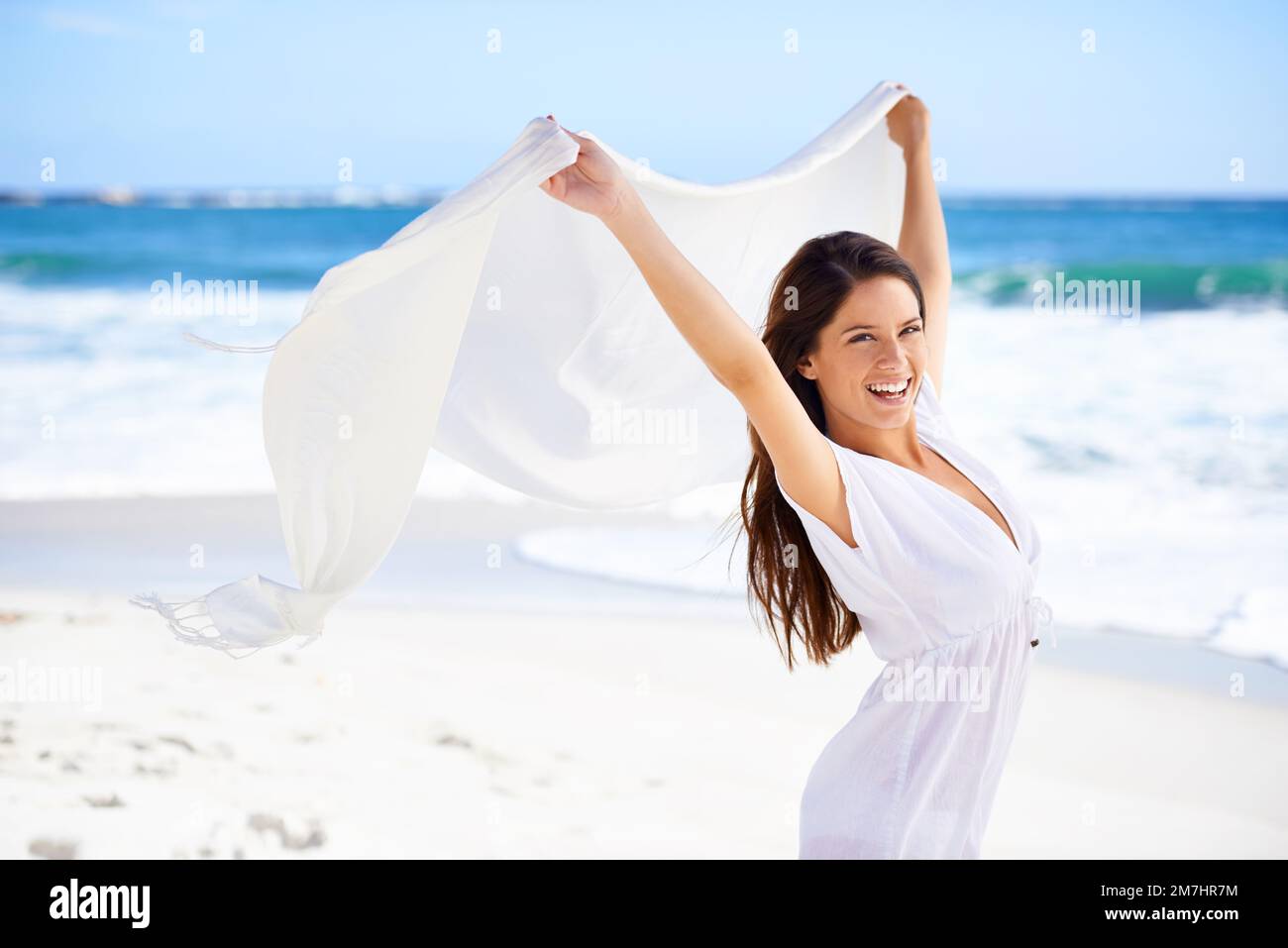 Sommerstil. Eine wunderschöne junge Frau am Strand mit einem weißen Schal, der im Wind weht. Stockfoto